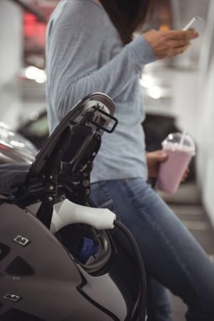 Car being charged with electric car charger while woman standing in background at electric vehicle charging station